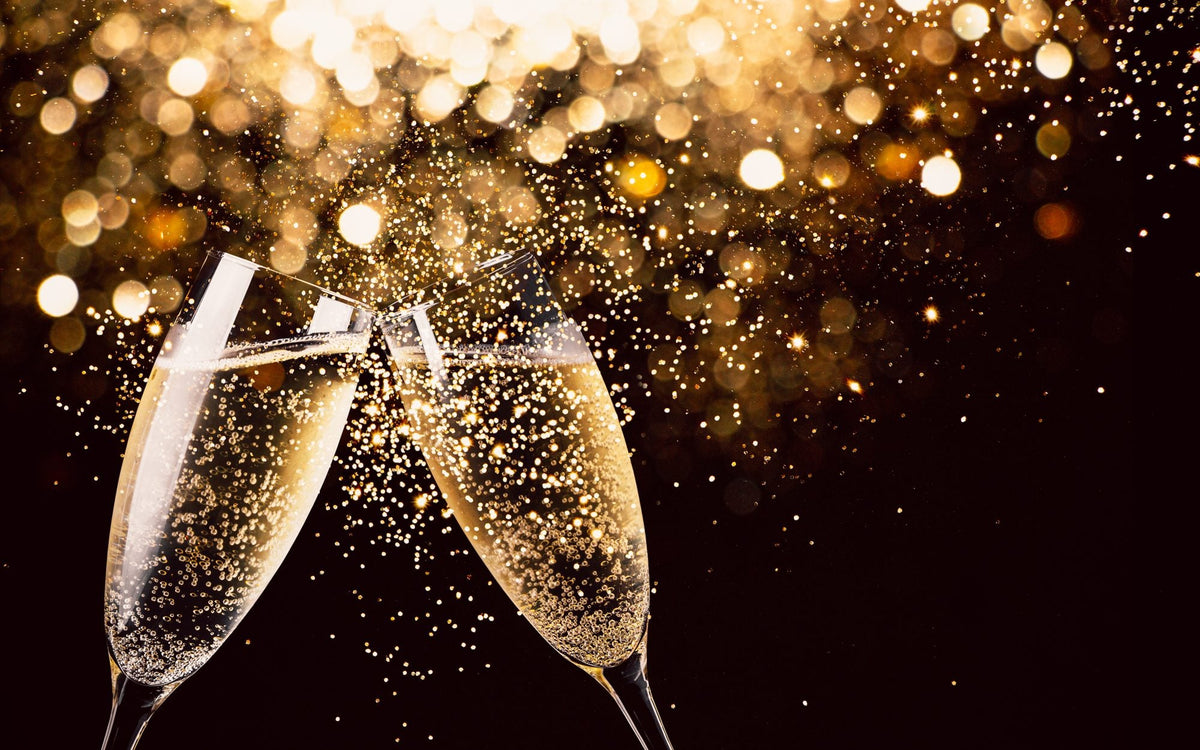 Two glasses of sparkling wine clinking against gold Christmas lights
