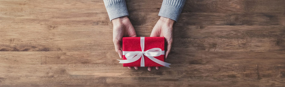 Hands holding a small red gift over a wooden table