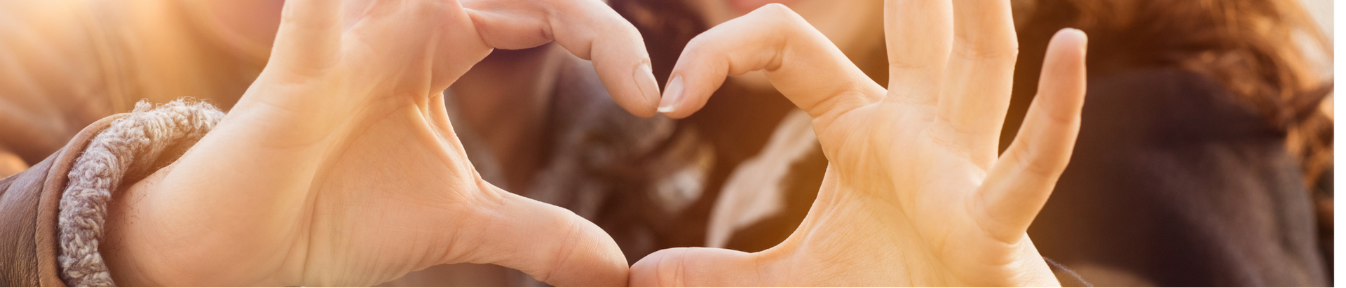 Close-up of two hands forming a heart shape against a warm, sunlit background, suggesting love, care, or connection.