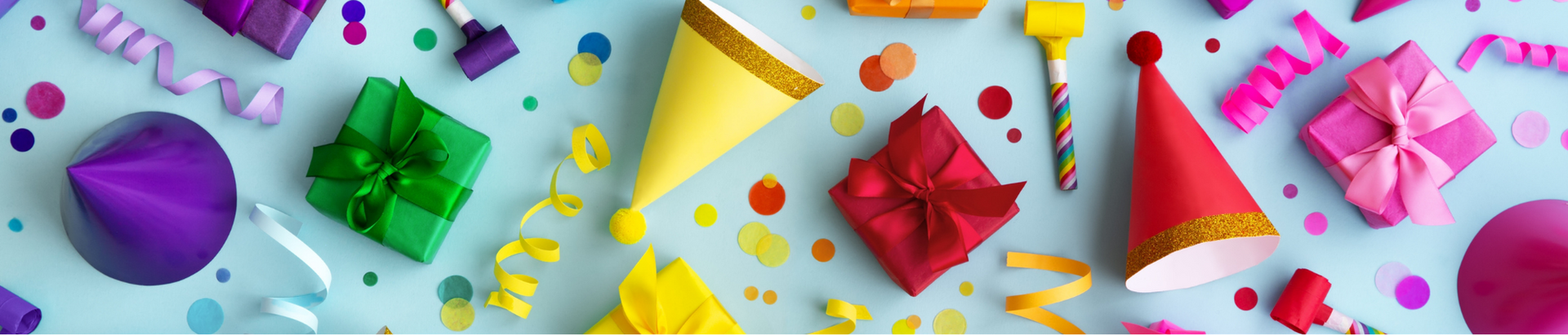 Colorful party hats, wrapped gifts with ribbons, confetti, and party blowers scattered on a light blue background, creating a festive celebration scene.