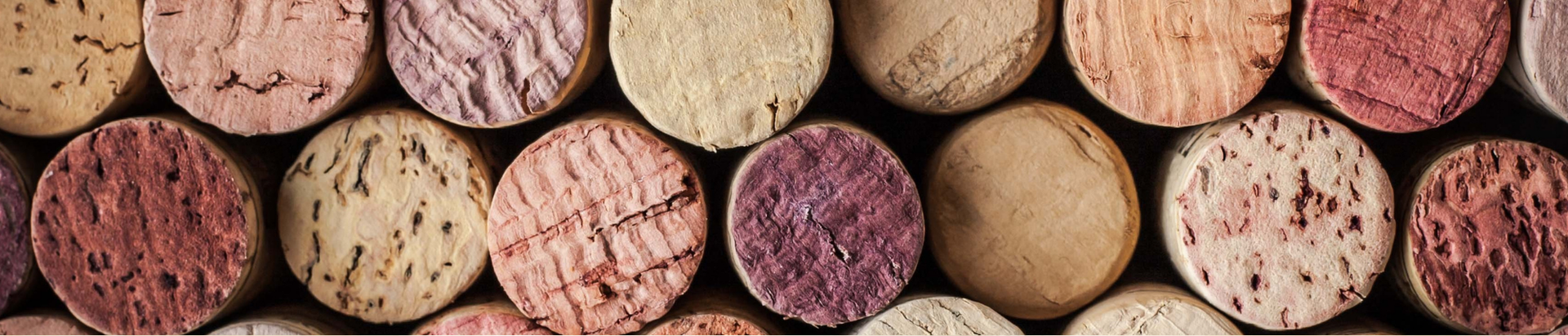 A close-up of several wine corks arranged side by side, showing their textured tops in various shades of beige, pink, and purple.