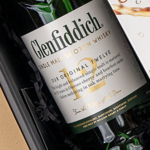Close-up of a Glenfiddich Explorer's Hamper by The Hamper Boutique Co, featuring the 12 in gold on the whisky label and descriptive text about its maturation in Dufftown, Scotland, nestled among black crinkle paper.