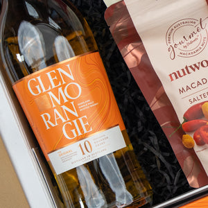 The Hamper Boutique Co Glenmorangie Moments Hamper features a Glenmorangie 10-year-old whisky in a gift box paired with Nutworks salted macadamia nuts on black shredded paper.