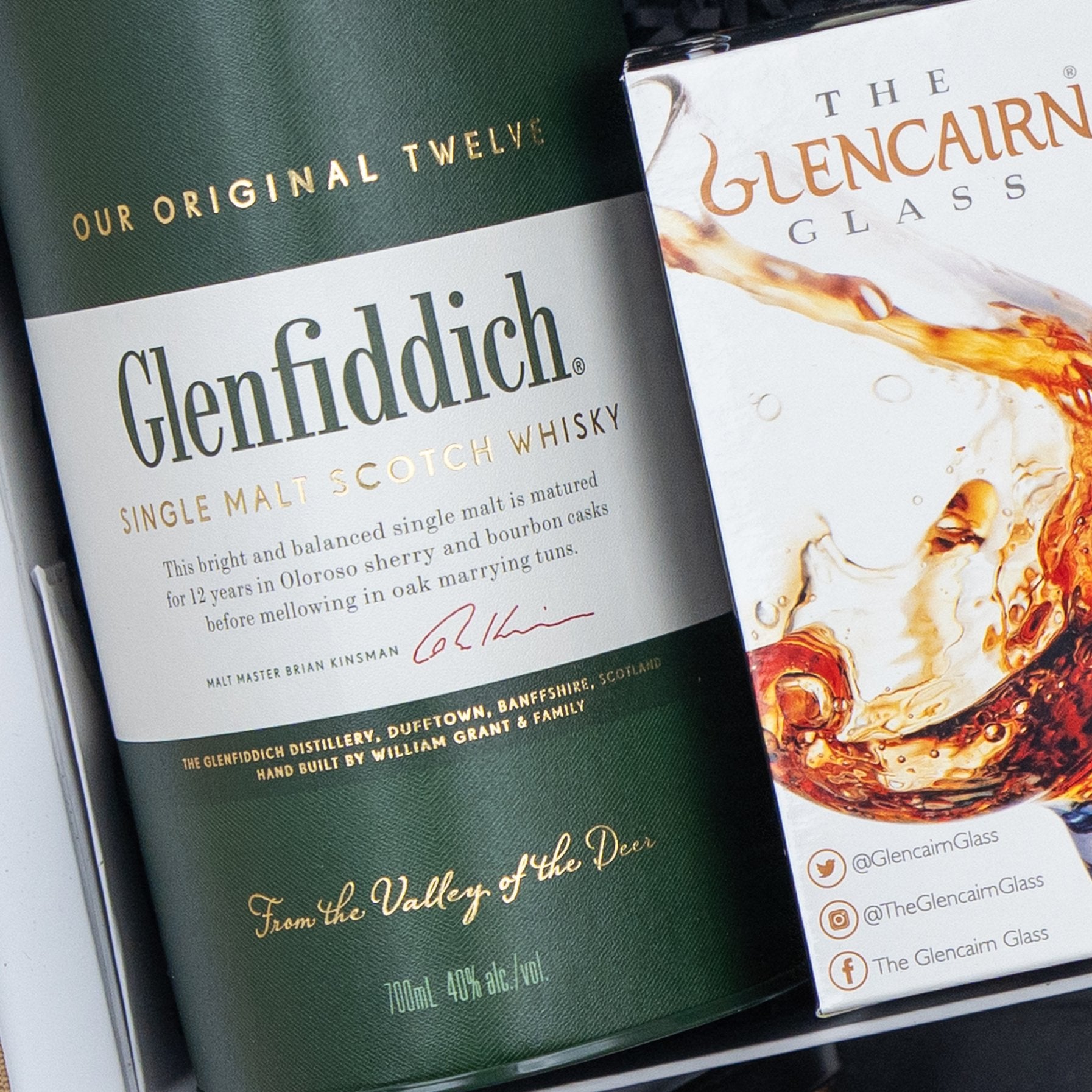 A Glenfiddich Connoisseur's Hamper from The Hamper Boutique Co sits beside a partially visible Glencairn Glass box featuring a splash of whisky on its packaging.