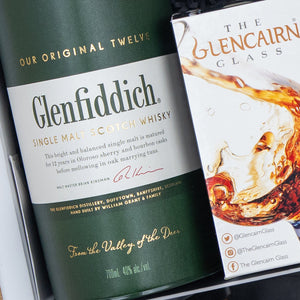 A Glenfiddich Connoisseur's Hamper from The Hamper Boutique Co sits beside a partially visible Glencairn Glass box featuring a splash of whisky on its packaging.