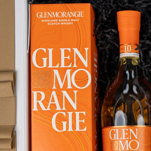 The Glenmorangie Discovery Hamper by The Hamper Boutique Co features a bottle of Glenmorangie Highland Single Malt Scotch Whisky in orange packaging, elegantly presented in a gift box with black shredded paper.