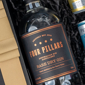 The Hamper Boutique Co’s Four Pillars Discovery Hamper features a bottle of Four Pillars Rare Dry Gin in a black and copper label, presented in a gift box with shredded black paper and assorted beverage cans.
