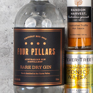 A close-up of The Hamper Boutique Co’s Four Pillars Premium Gin Hamper, featuring a gin bottle, Random Harvest Australian Truffle Hot Sauce, and Fever-Tree Indian Tonic Water can against a textured gray background.