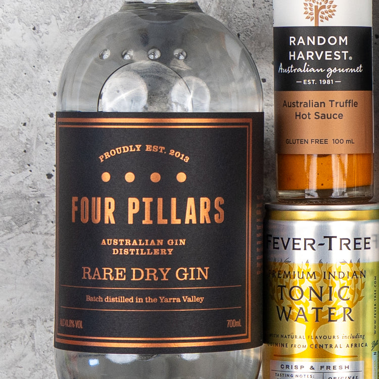 A close-up of The Hamper Boutique Co’s Four Pillars Premium Gin Hamper, featuring a gin bottle, Random Harvest Australian Truffle Hot Sauce, and Fever-Tree Indian Tonic Water can against a textured gray background.