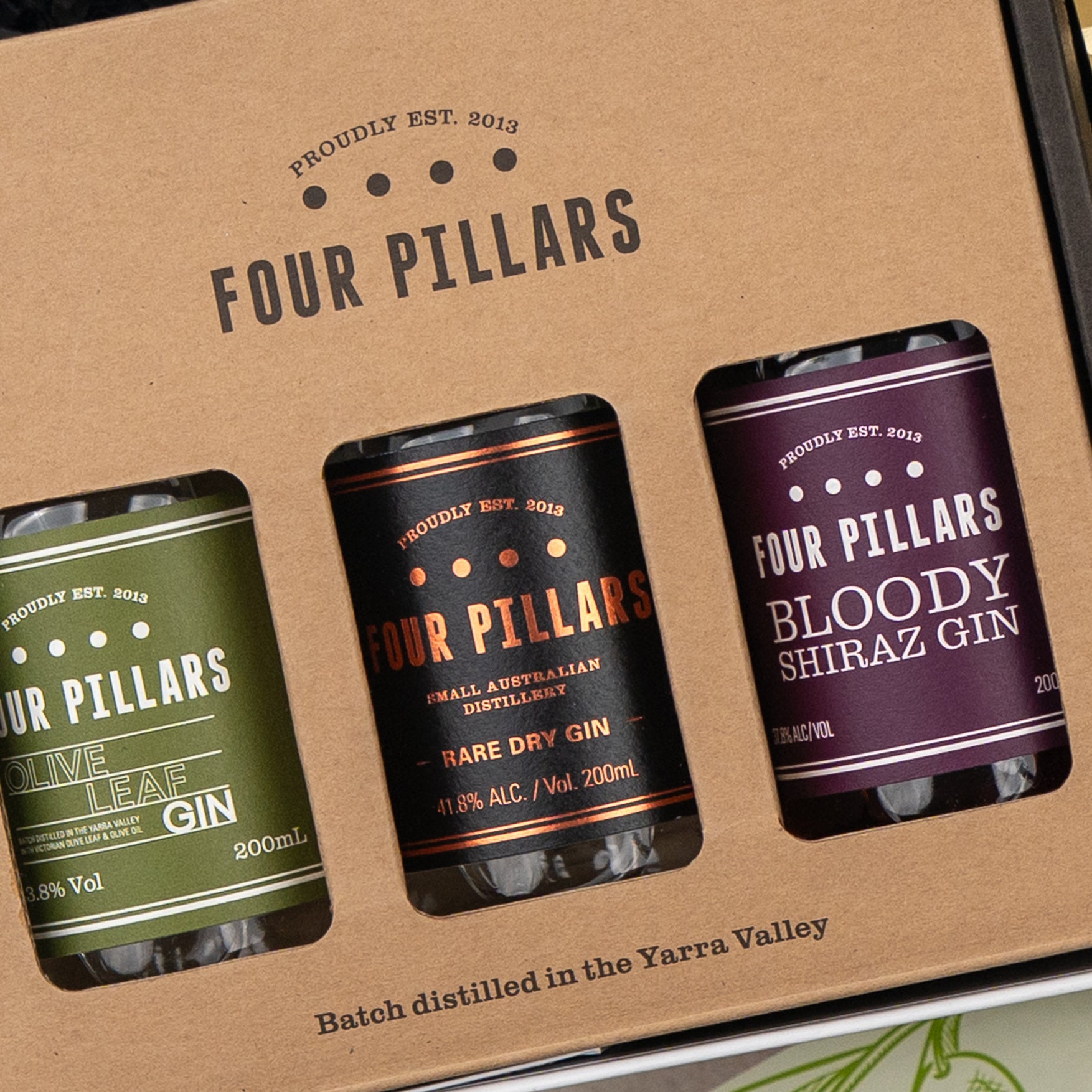 A close-up of The Hamper Boutique Co's Four Pillars Botanical Discovery Hamper featuring three labeled mini bottles—Olive Leaf Gin, Rare Dry Gin, and Bloody Shiraz Gin—neatly arranged in a gift box with cut-out slots.