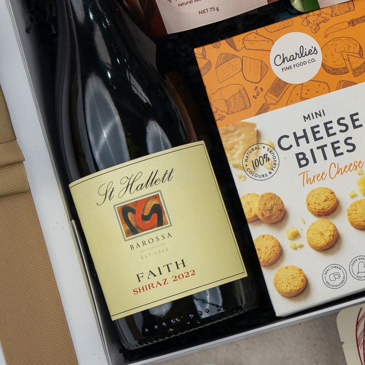 A close-up of The Hamper Boutique Co Red Wine Gourmet Collection Hamper featuring a bottle of wine and gourmet cheese bites.