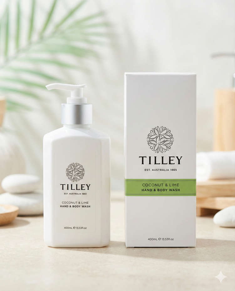 A white pump bottle labeled Tilley Coconut and Lime Body Wash stands beside its matching box on a light surface, with smooth stones and soft-focus greenery in the background.