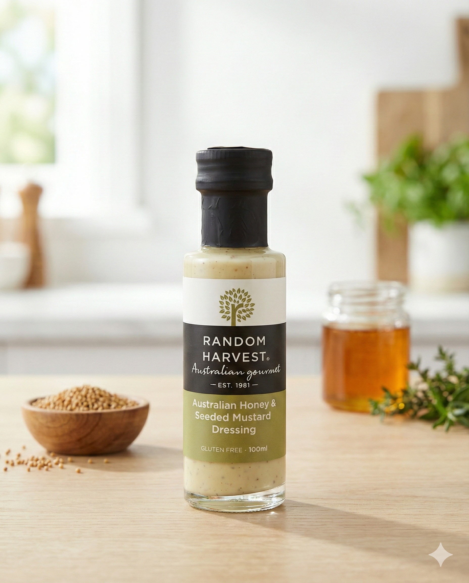 A bottle of Random Harvest Australian Honey and Seeded Mustard Dressing is on a kitchen counter, with a jar of honey, a bowl of mustard seeds, and a green plant visible in the blurred background.
