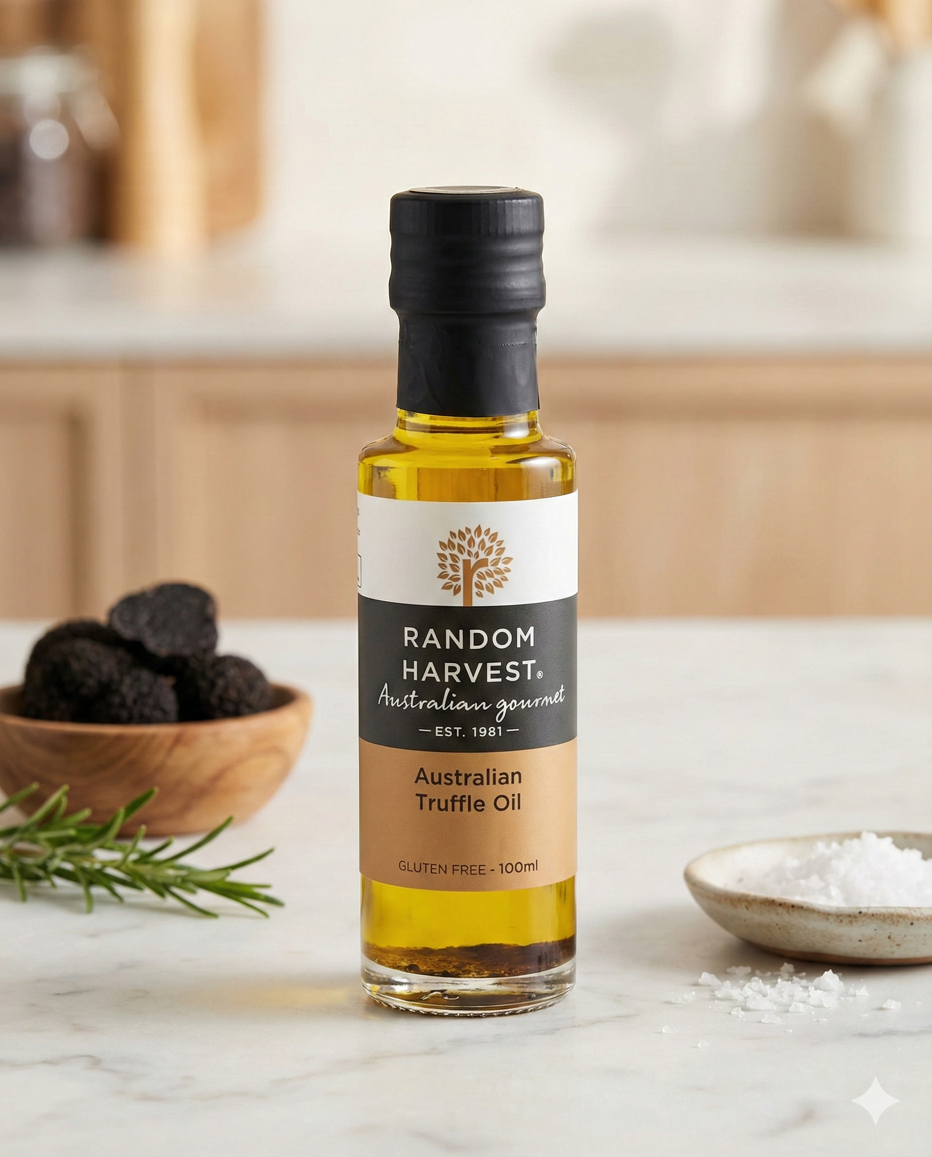 A bottle of Random Harvest Australian Truffle Oil rests on a white countertop, accompanied by truffles, rosemary, and coarse salt, with a softly blurred background.
