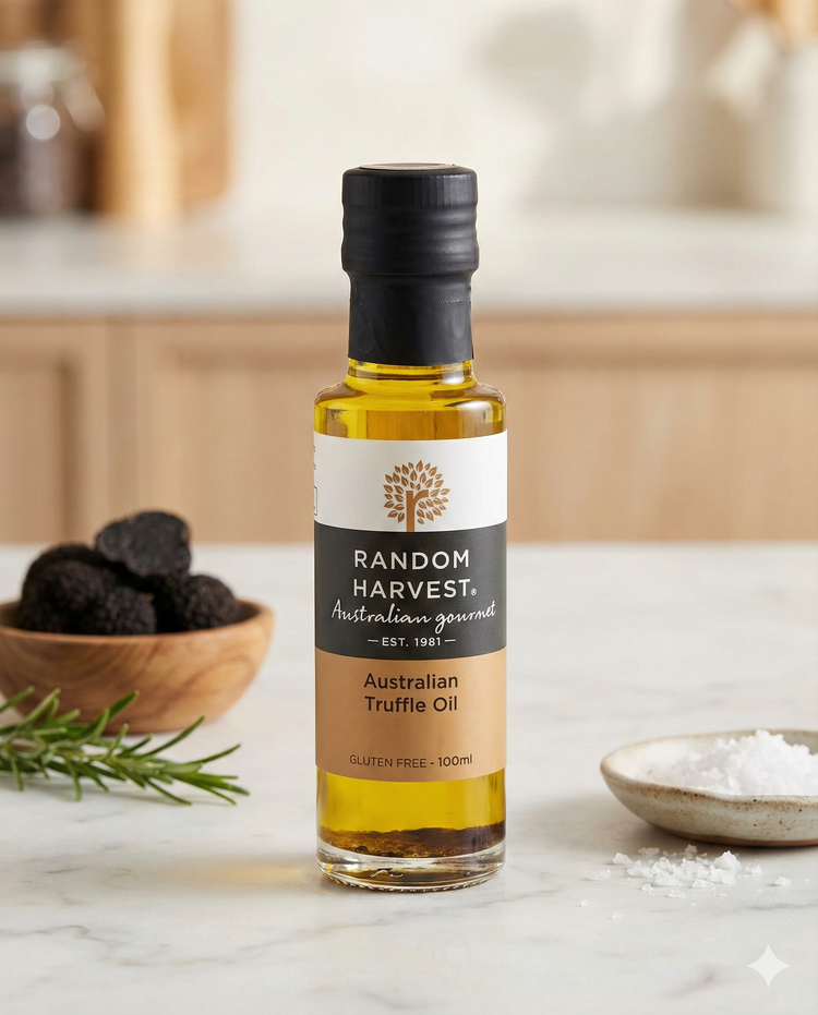 A bottle of Random Harvest Australian Truffle Oil rests on a white countertop, accompanied by truffles, rosemary, and coarse salt, with a softly blurred background.