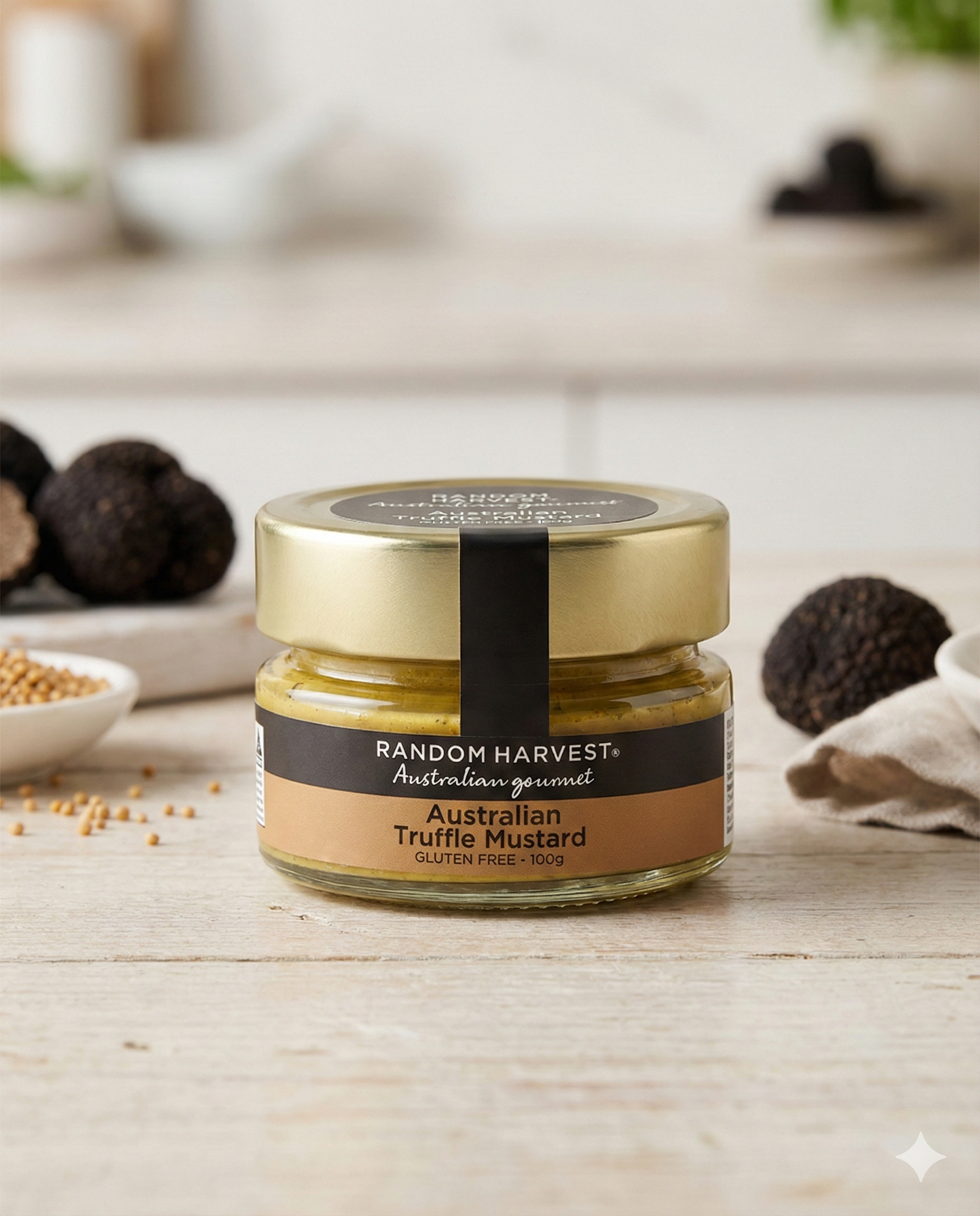 A glass jar of Random Harvest Australian Truffle Mustard with a gold lid rests on a light wooden surface, surrounded by truffles, mustard seeds, and a white cloth in a kitchen setting.