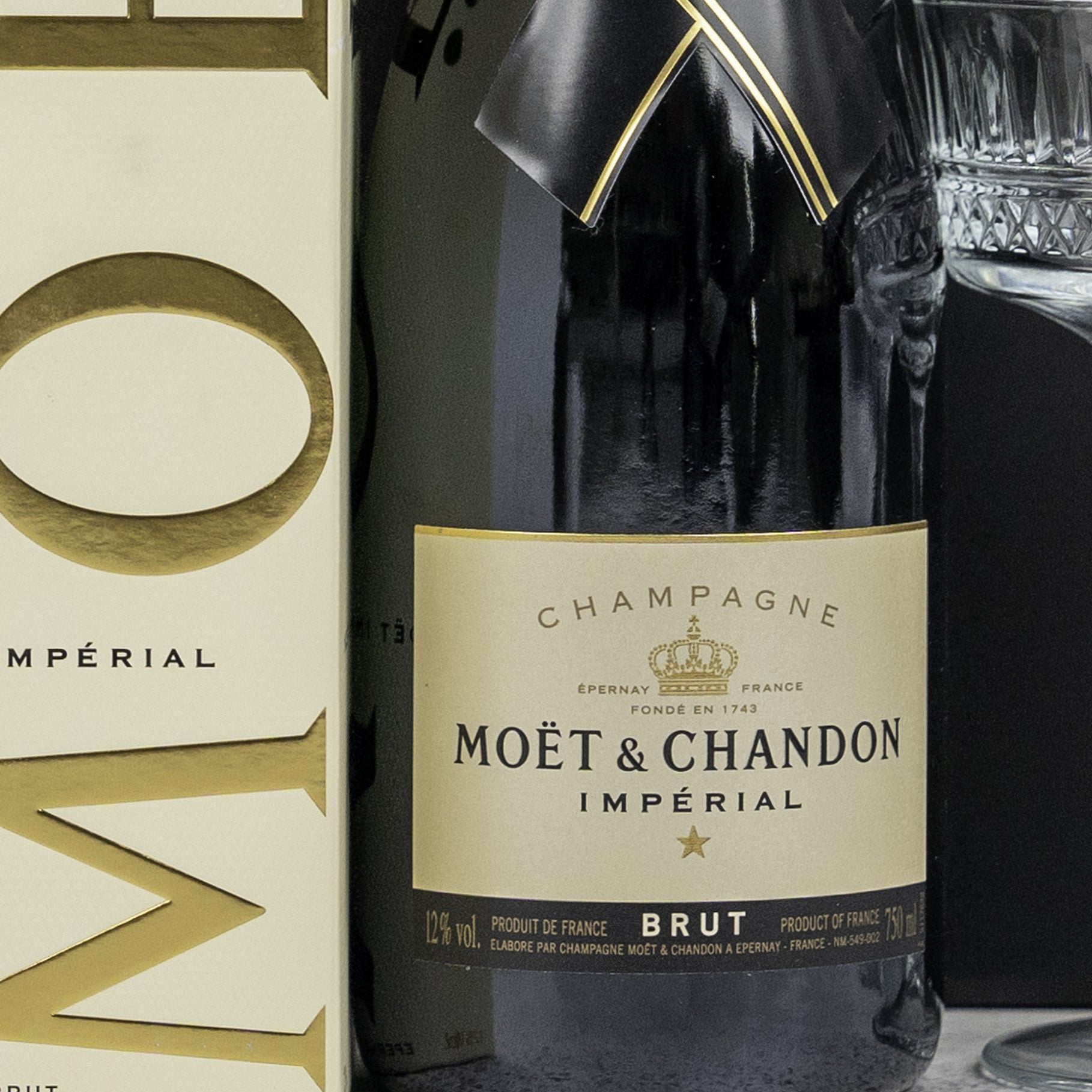 A Gin and Homeware Essentials Hamper by The Hamper Boutique Co is displayed next to its matching box, with a partially visible glass in the background.