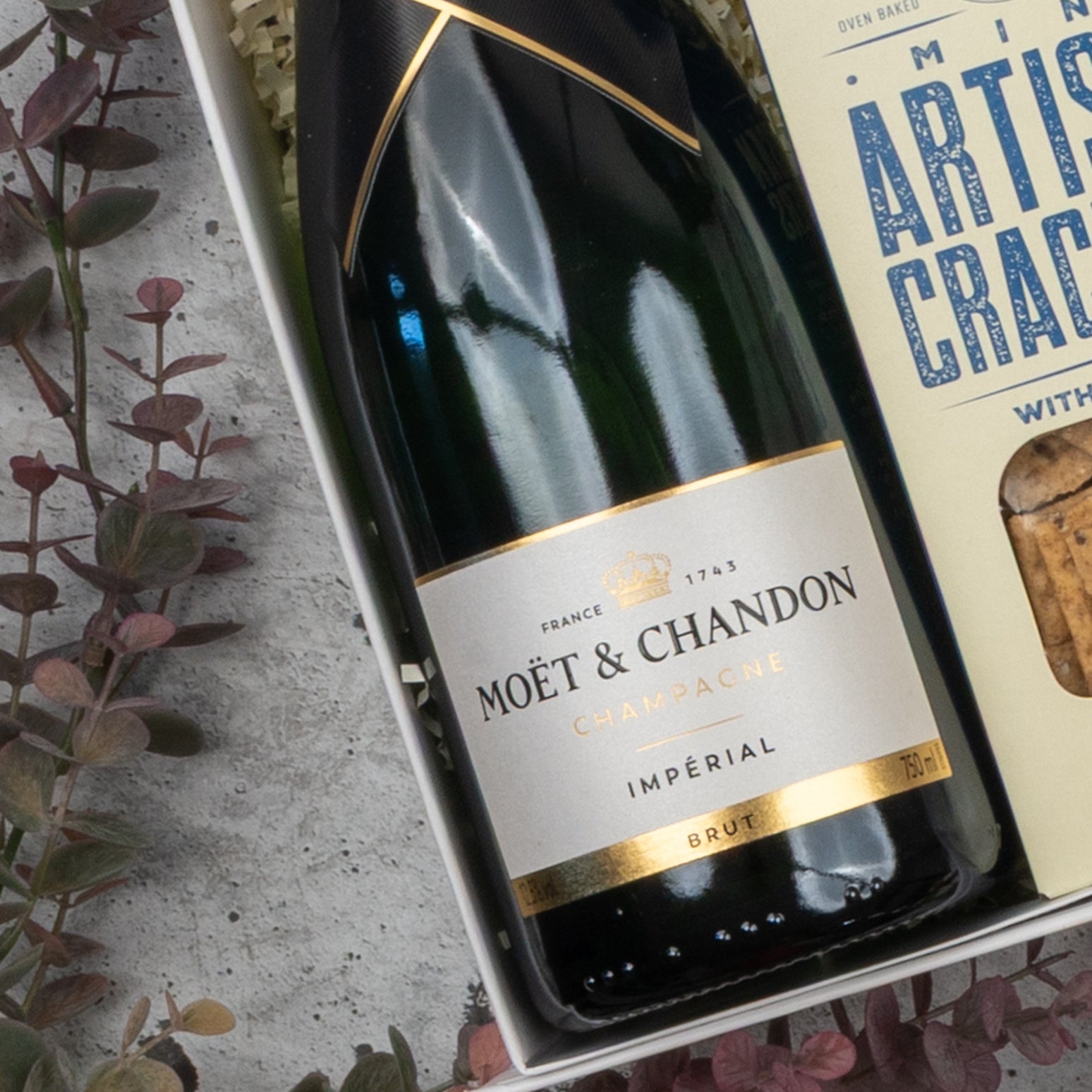 The Hamper Boutique Co's Moët & Chandon Premium Celebration Hamper features a bottle of champagne and artisan crackers, beautifully arranged in a decorative gift box with foliage.