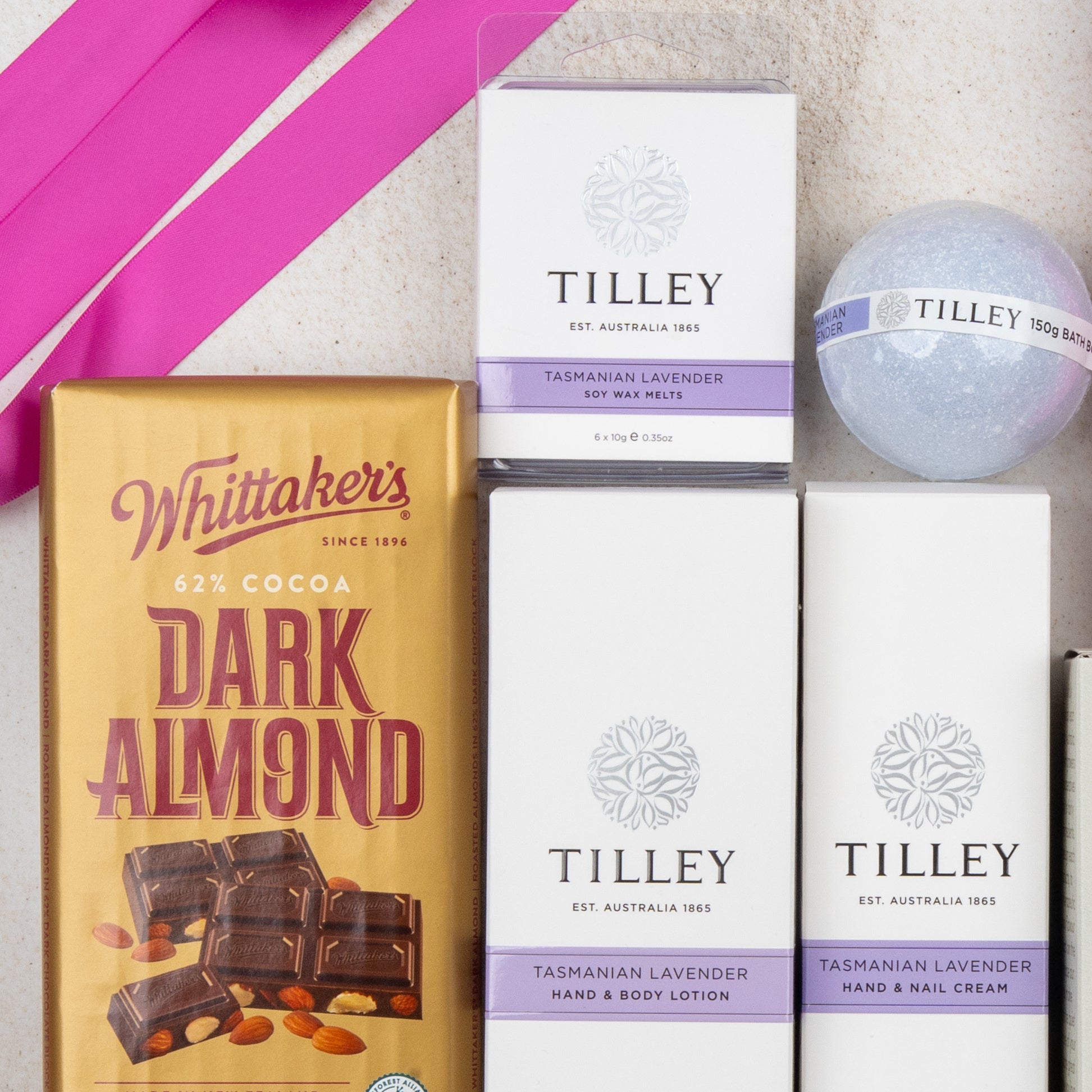 A flat lay of The Hamper Boutique Co’s Rejuvenation and Wellness Hamper, featuring luxurious bath and body products, on a light surface with pink ribbon.