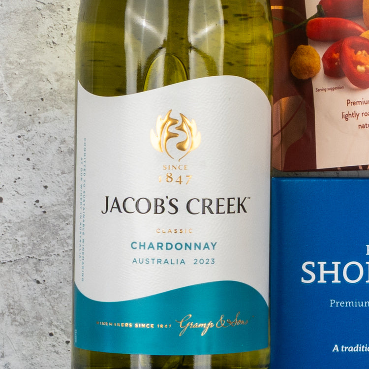 A Gourmet Getaway Gift Hamper by The Hamper Boutique Co is placed on a light stone surface, beside a blue rectangular item and part of a red-labeled food package.