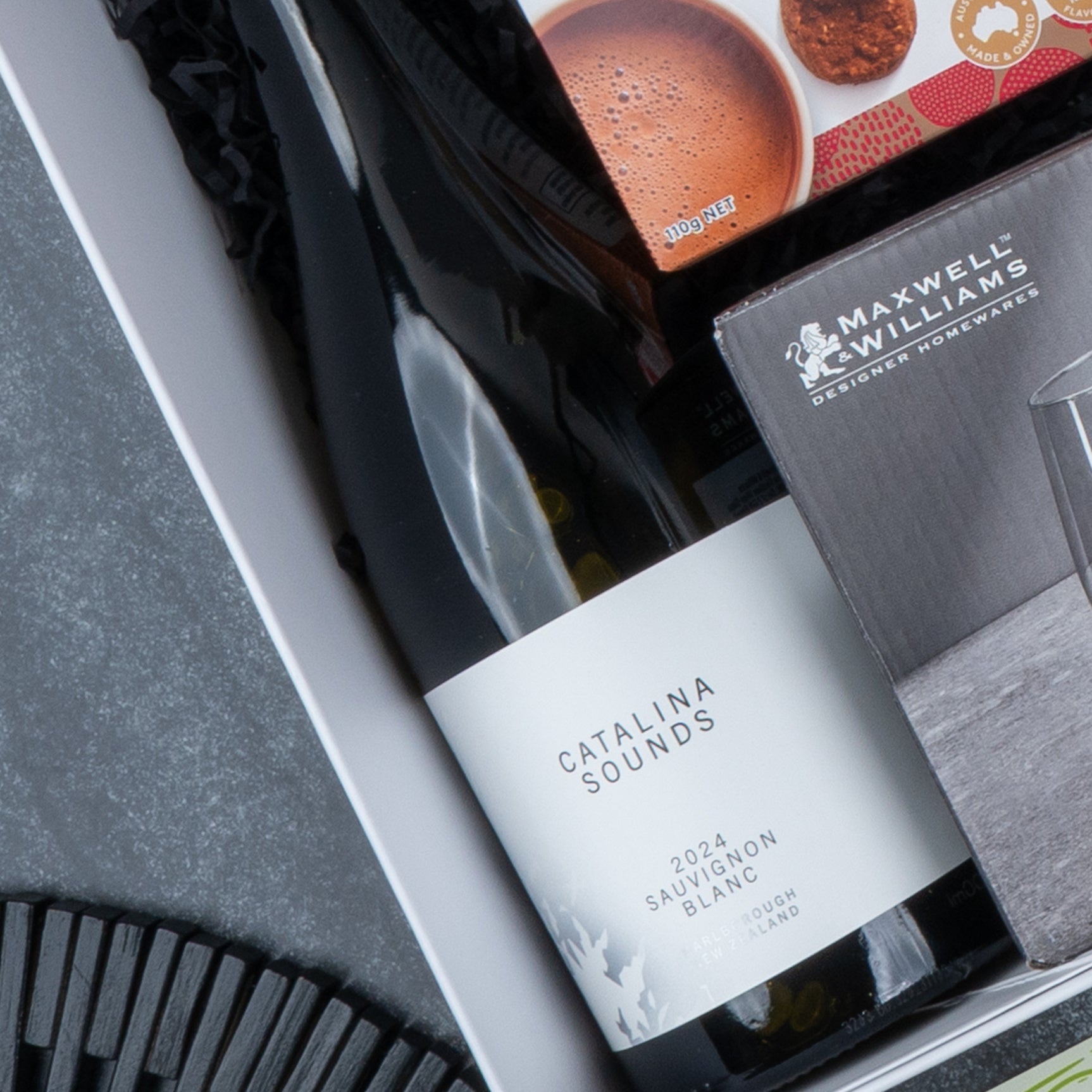 The Hamper Boutique Co Epicurean Delights Hamper includes a Catalina Sounds 2021 Sauvignon Blanc, Maxwell & Williams glassware, and a cookie package—perfect for gifting.