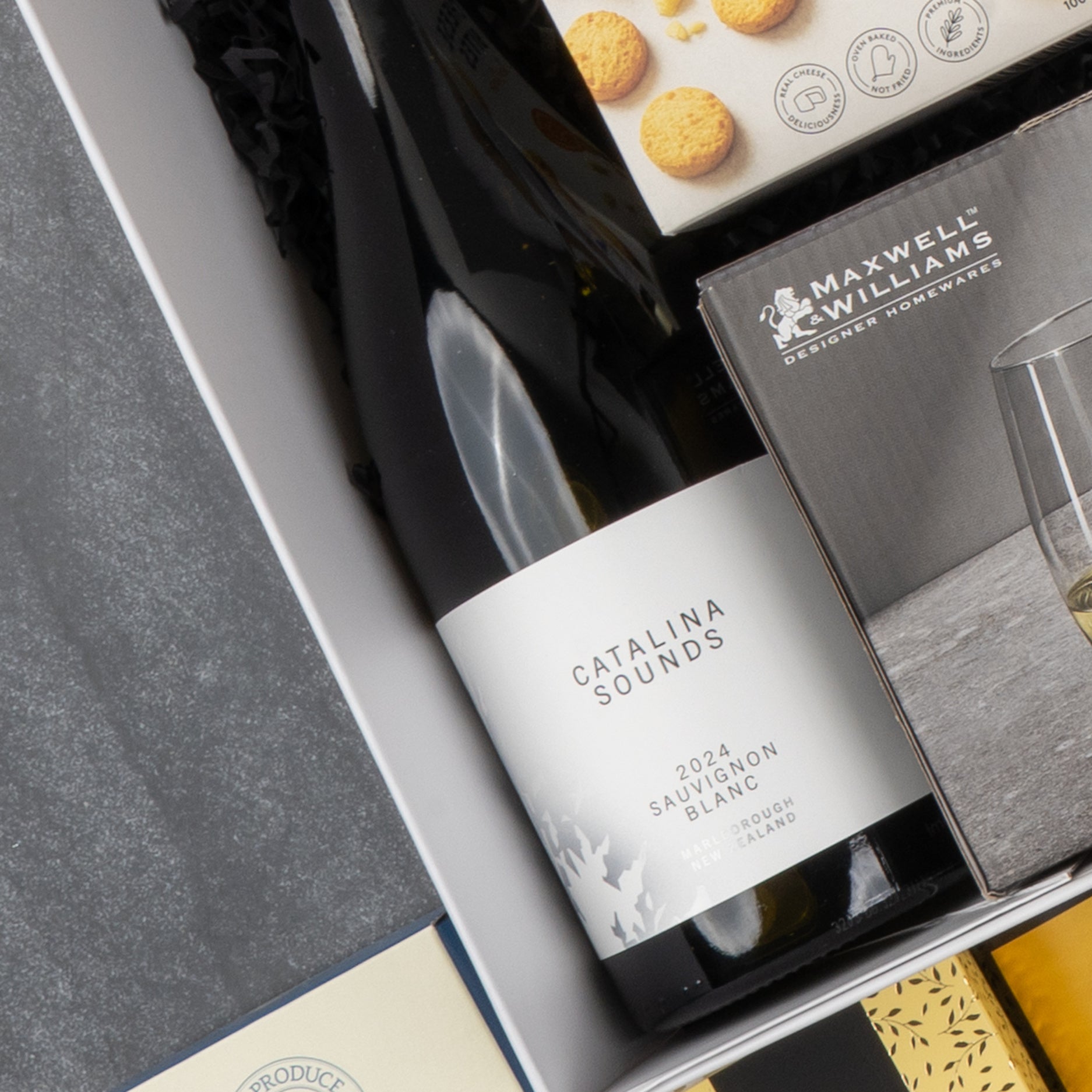 A close-up of The Hamper Boutique Co's Gourmet Collection Gift Hamper, featuring Catalina Sounds 2024 Sauvignon Blanc, Maxwell & Williams glasses, and assorted gourmet treats in elegant packaging.