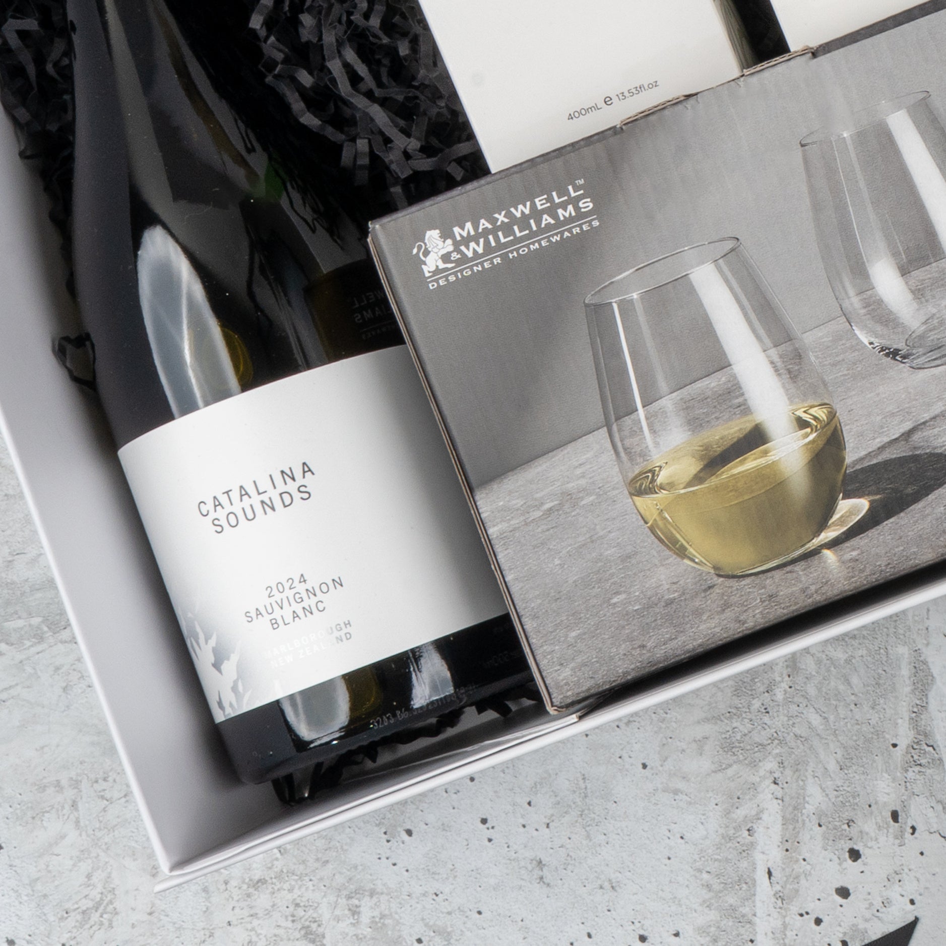 The Hamper Boutique Co’s Elegance and Self-Care Gift Hamper includes Catalina Sounds 2024 Sauvignon Blanc and Maxwell & Williams stemless wine glasses, beautifully presented in a gift box with black crinkle paper.