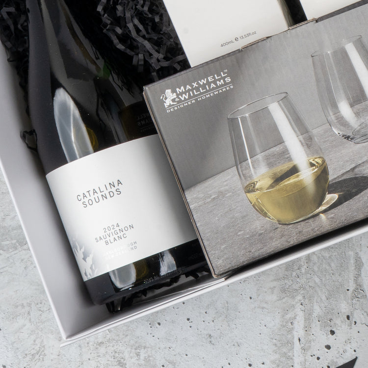 The Hamper Boutique Co’s Elegance and Self-Care Gift Hamper includes Catalina Sounds 2024 Sauvignon Blanc and Maxwell & Williams stemless wine glasses, beautifully presented in a gift box with black crinkle paper.