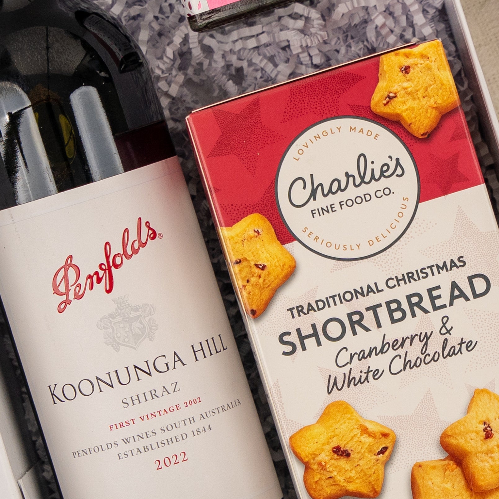 A Merry Shiraz Moments gift hamper from The Hamper Boutique Co featuring Penfolds Koonunga Hill Shiraz 2022 and Charlies Traditional Christmas Shortbread with cranberry and white chocolate, elegantly presented on shredded paper.