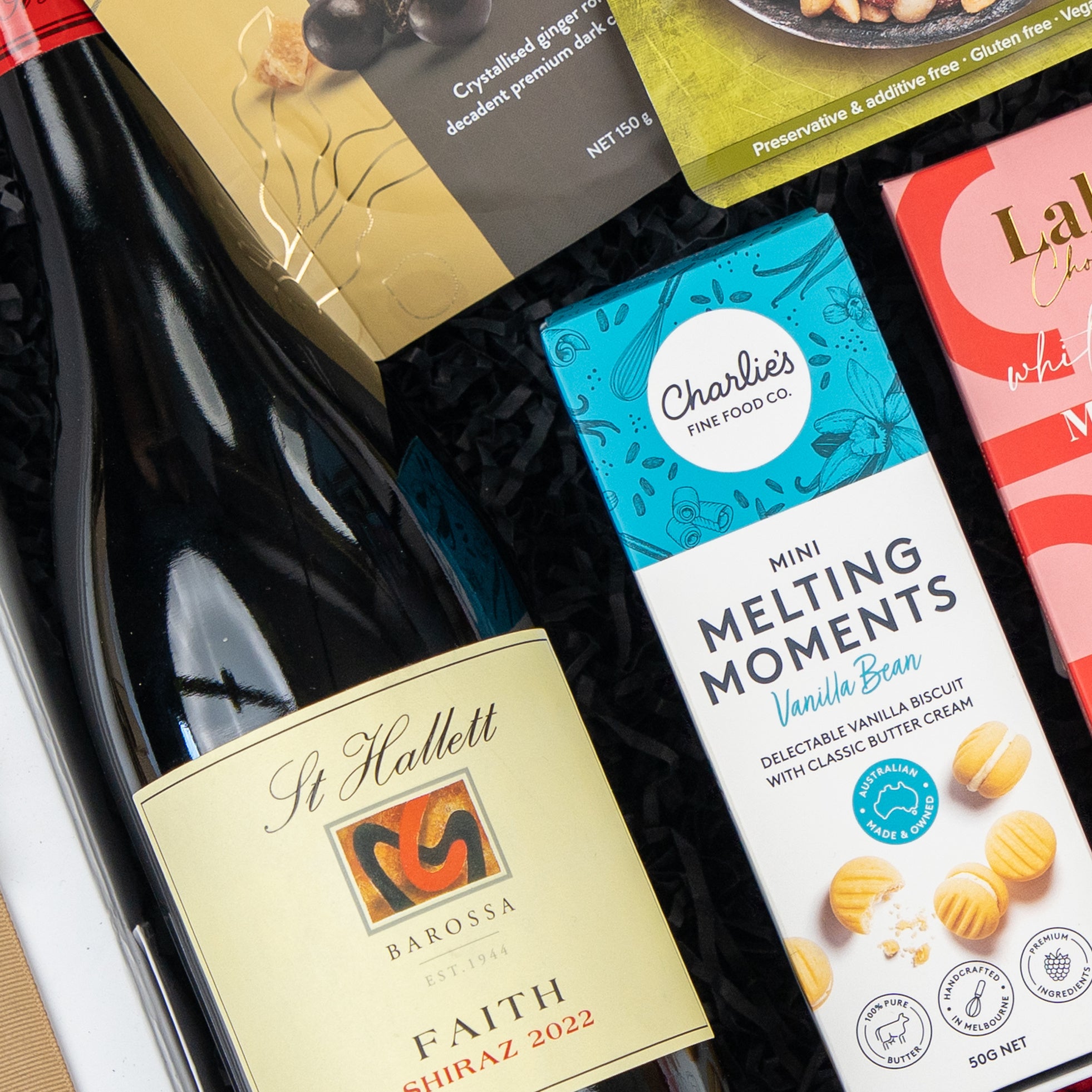 A close-up of the Gourmet Gathering hamper by The Hamper Boutique Co, featuring St Hallett Shiraz 2022, Charlies Melting Moments vanilla bean biscuits, and assorted gourmet snacks.