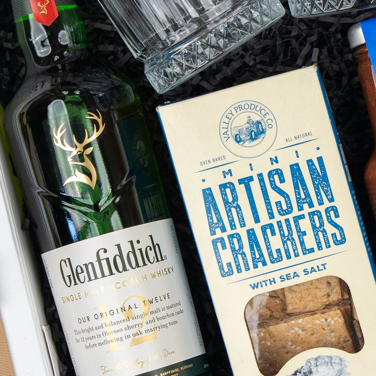 The Whisky Wonder gift box by The Hamper Boutique Co features Glenfiddich Scotch whisky and Valley Produce Co. Mini Artisan Crackers with Sea Salt, presented with glassware and other packaged treats.