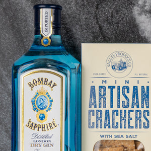 The Hamper Boutique Co's Bombay Sapphire Gin and Tonic Hamper sits beside a box of Valley Produce Co. mini artisan sea salt crackers on a dark stone surface.