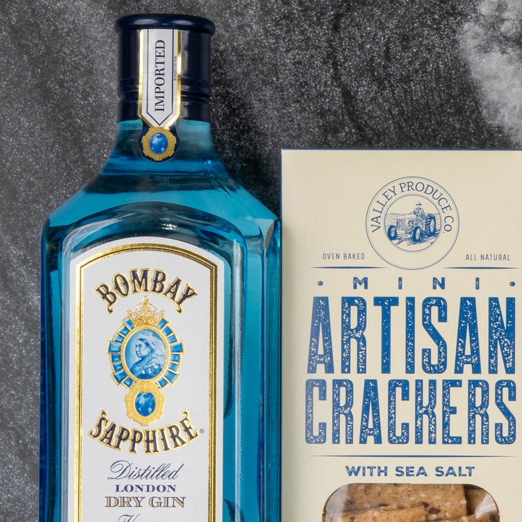 The Hamper Boutique Co's Bombay Sapphire Gin and Tonic Hamper sits beside a box of Valley Produce Co. mini artisan sea salt crackers on a dark stone surface.
