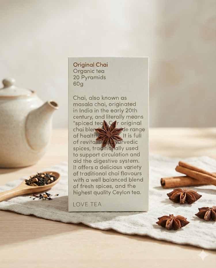A box of Love Tea Original Chai rests on a wooden surface with star anise, surrounded by a teapot, a bowl of loose tea, and scattered spices like star anise.