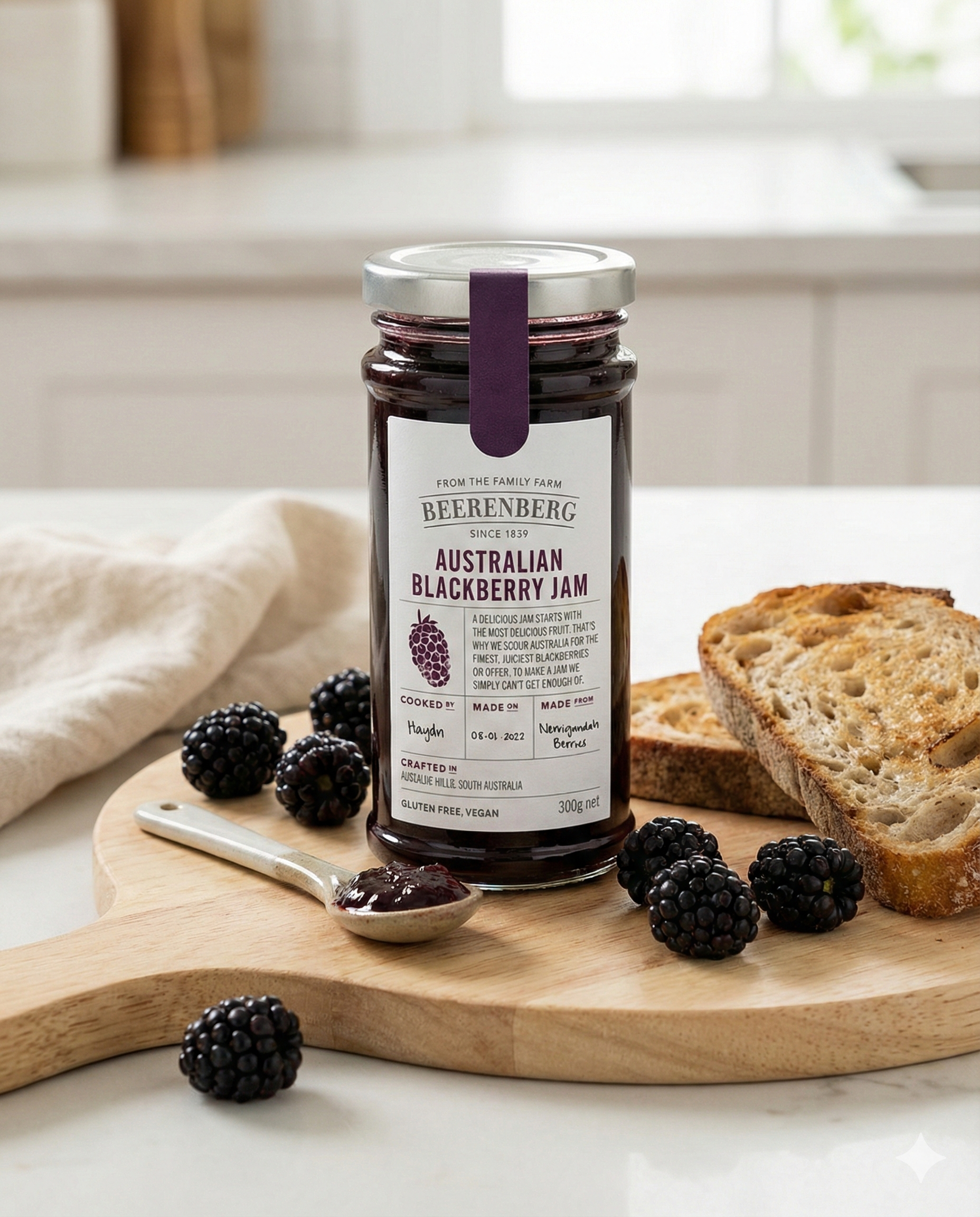 A jar of Beerenberg Blackberry Jam sits on a table with a spoonful of jam, fresh blackberries, and toasted bread slices arranged beside it.