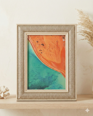 The Australian House & Garden Linen Look Photo Frame showcases an aerial coastline photo, featuring vivid orange land meeting turquoise water, styled on a shelf with decorative coral and dried grass in the background.