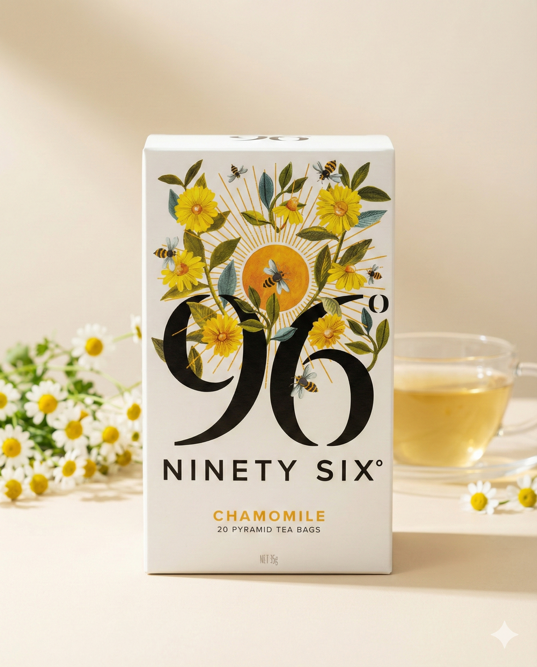 A box of 96 Degrees Chamomile Tea with floral and bee designs is displayed on a light surface, accompanied by a glass cup of chamomile tea and chamomile flowers in the background.