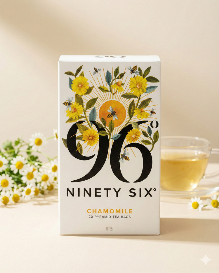 A box of 96 Degrees Chamomile Tea with floral and bee designs is displayed on a light surface, accompanied by a glass cup of chamomile tea and chamomile flowers in the background.