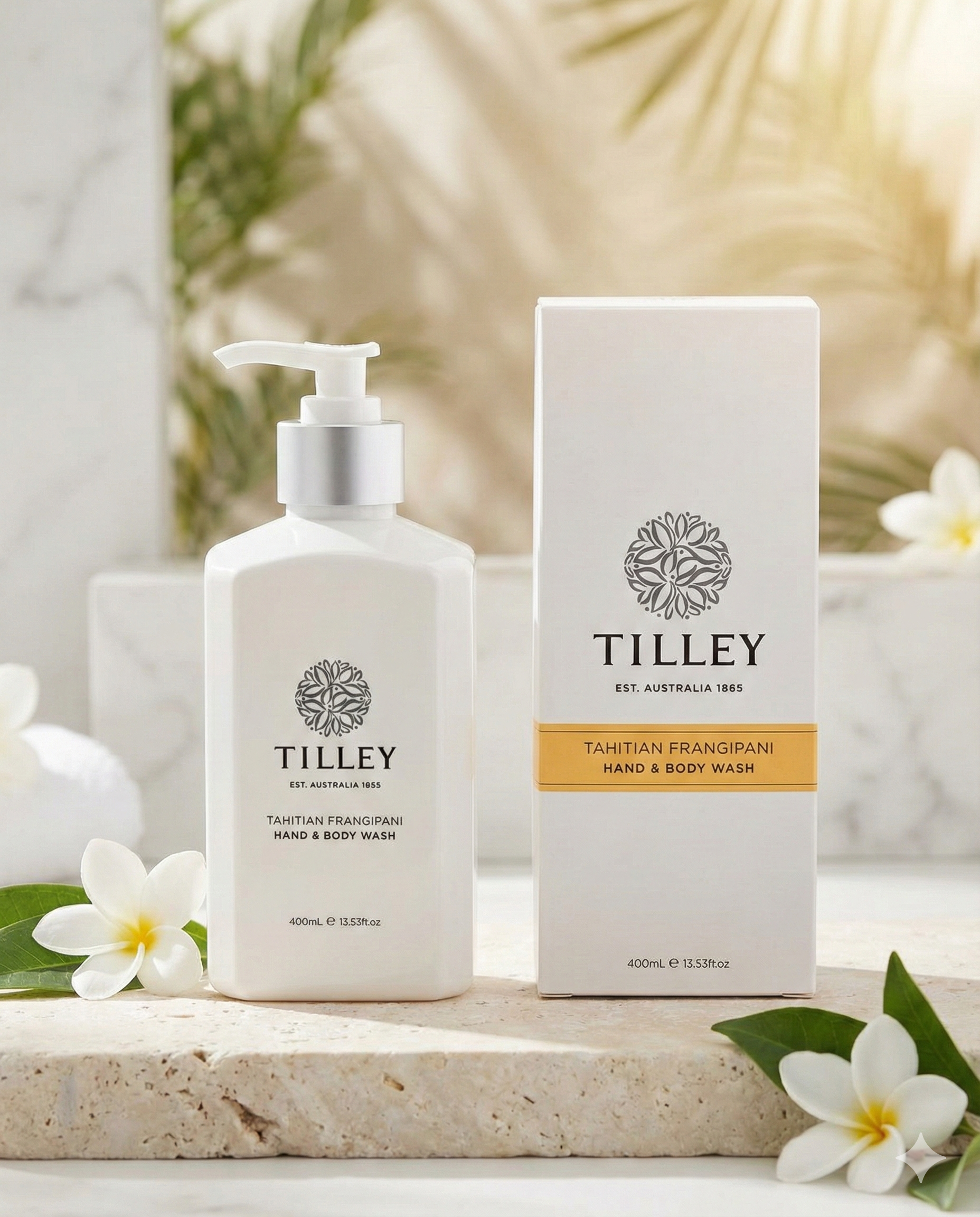 A bottle and box of Tilley Tahitian Frangipani Hand and Body Wash sit on a stone surface, accented by white frangipani flowers and bathed in gentle natural light.