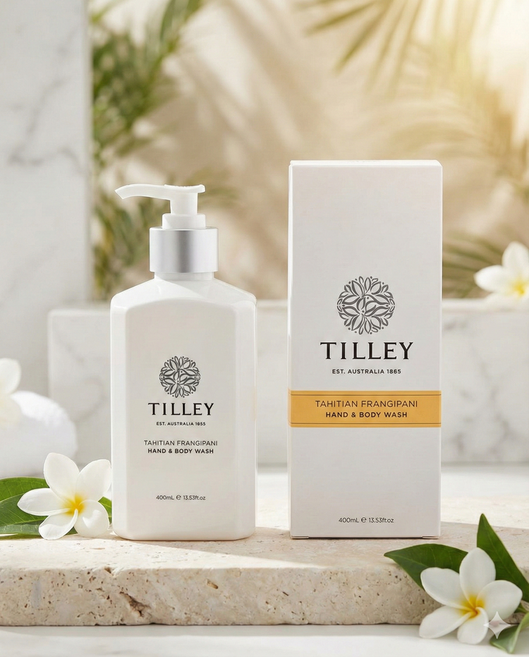 A bottle and box of Tilley Tahitian Frangipani Hand and Body Wash sit on a stone surface, accented by white frangipani flowers and bathed in gentle natural light.