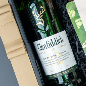 The Glenfiddich Tasting Hamper by The Hamper Boutique Co features a bottle of Glenfiddich Single Malt Scotch Whisky in a gift box with black shredded paper, plus part of the tan textured cover and green packaging.