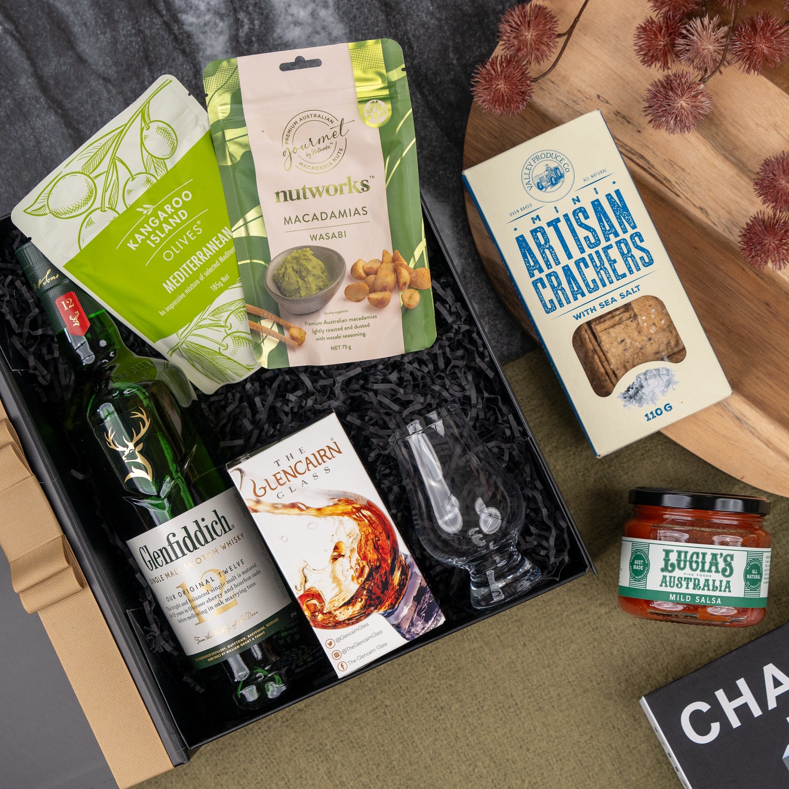 The Glenfiddich Explorer's Hamper by The Hamper Boutique Co features Glenfiddich whisky, two Glencairn glasses, wasabi macadamias, artisan crackers, marinated olives, and Luigi’s Australia mild salsa, elegantly arranged.
