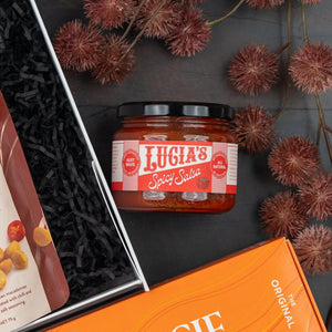 A Glenmorangie Moments Hamper by The Hamper Boutique Co rests on a dark surface, surrounded by decorative brown seed pods and partially visible food packages.