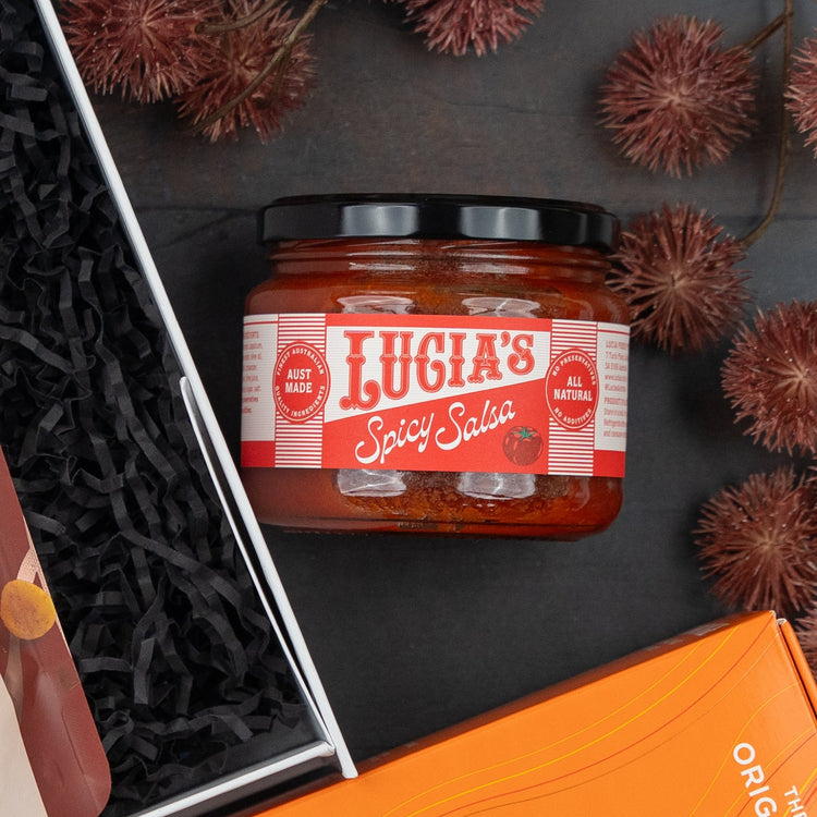 A Glenmorangie Moments Hamper by The Hamper Boutique Co sits on a dark surface, surrounded by a gift box filled with black shredded paper and decorated with brown pom-pom accents.