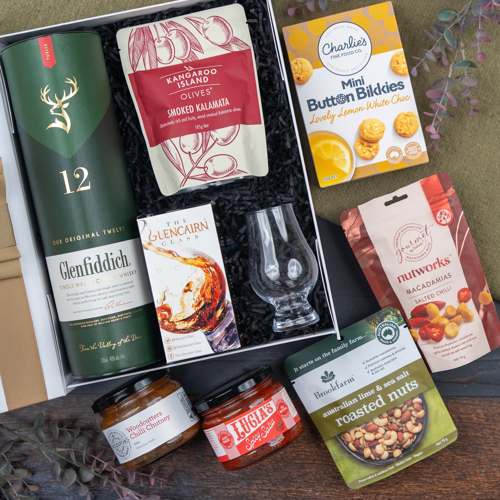 The Hamper Boutique Co Glenfiddich Connoisseur's Hamper features Glenfiddich 12 whisky, a whisky glass, smoked Kalamata olives, mini white choc cookies, fruit cake, roasted nuts, salted macadamias, fig preserve & blood orange marmalade.