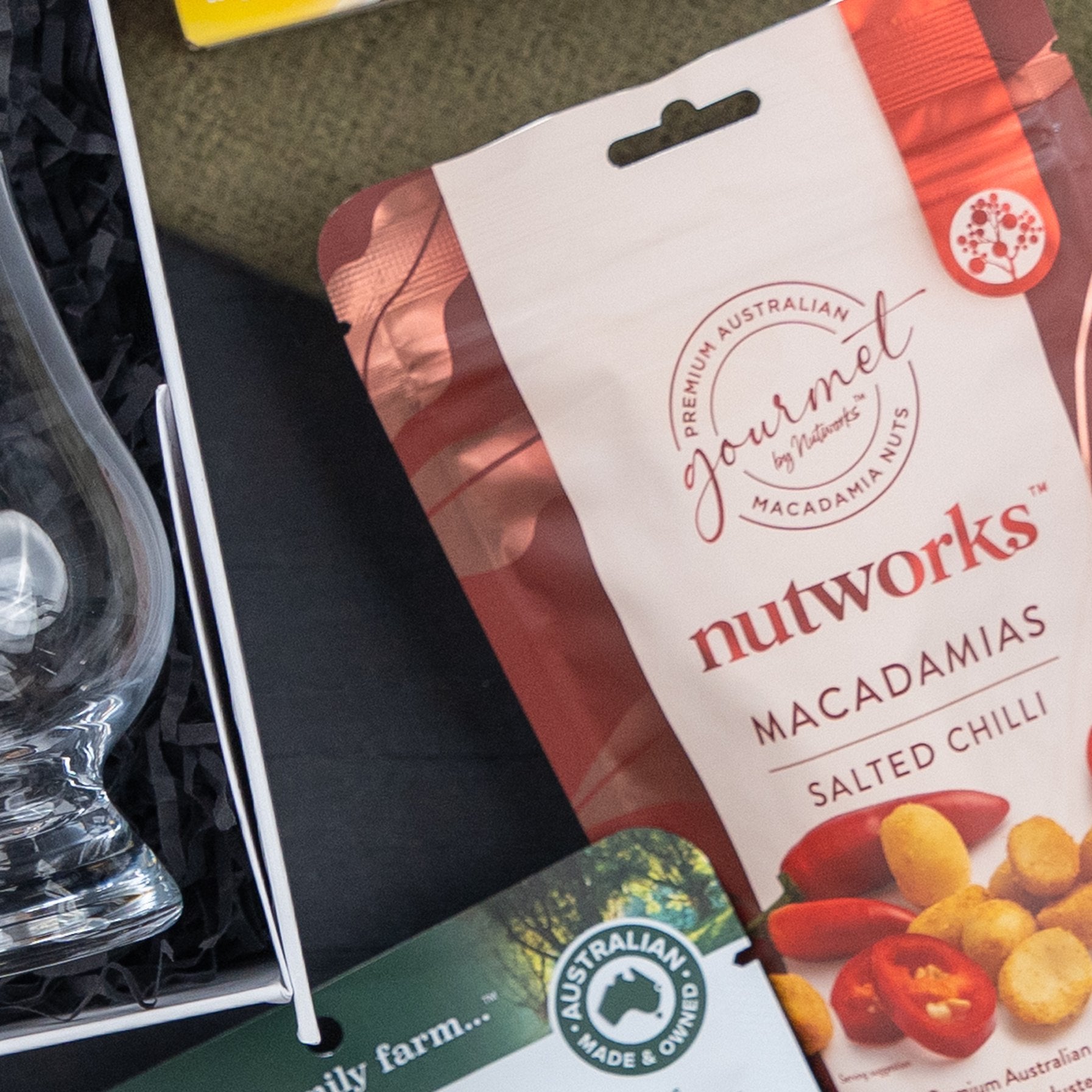 A Glenfiddich Connoisseur's Hamper by The Hamper Boutique Co rests beside a glass and an Australian Made & Owned card on a dark, textured surface.