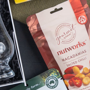 A Glenfiddich Connoisseur's Hamper by The Hamper Boutique Co rests beside a glass and an Australian Made & Owned card on a dark, textured surface.