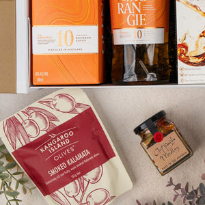 The Glenmorangie Discovery Hamper by The Hamper Boutique Co includes a bottle of Glenmorangie whisky, Kangaroo Island smoked kalamata olives, and a jar of Otways medley, beautifully arranged with decorative leaves.