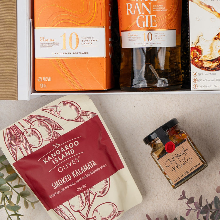 The Glenmorangie Discovery Hamper by The Hamper Boutique Co includes a bottle of Glenmorangie whisky, Kangaroo Island smoked kalamata olives, and a jar of Otways medley, beautifully arranged with decorative leaves.