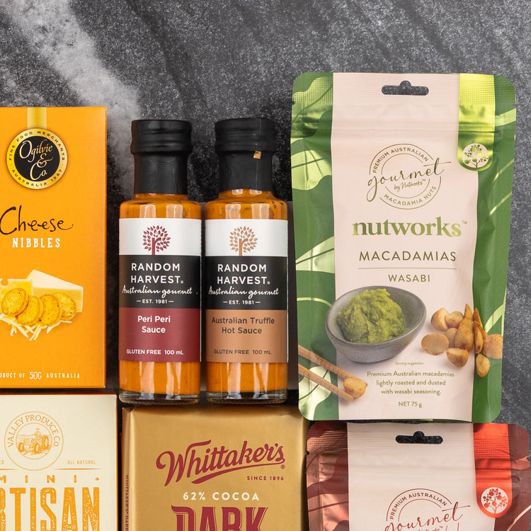 The Hamper Boutique Co’s Glenmorangie Tasting Experience Hamper features gourmet snacks on dark marble: cheese nibbles, two hot sauces, wasabi macadamias, crackers, and a bar of dark chocolate.